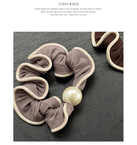 Detail of grey-purple scrunchie with cream pearl and white piping on black wood background
