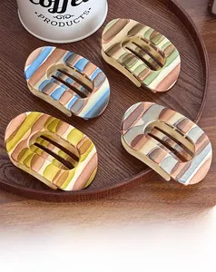 Macro view of four matte oval hair claws with colorful stripes in a wooden tray