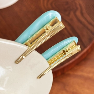 Elegant sky blue acetate hair clips with gold metal base displayed on a white plate