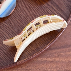 Frosted banana hair clip with retro abalone pattern on a warm wooden background