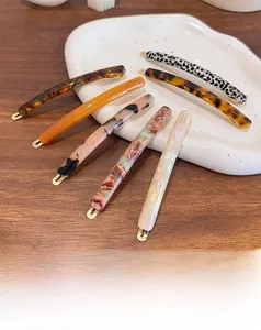Detailed close-up of acetate pattern hair clips with gold metal base and handmade lettering