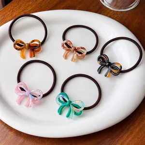 Close-up of acetic acid bow hair ties in amber, marble, and emerald on a ceramic tray