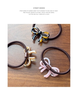 Three acetate bow hair ties in tortoiseshell, beige and pink on a dark wood surface