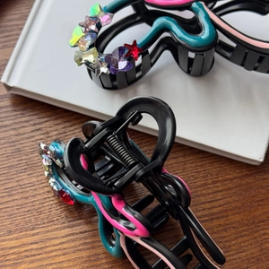 Elegant rhinestone bow claw clip with colorful oil-drip patterns on a white book surface