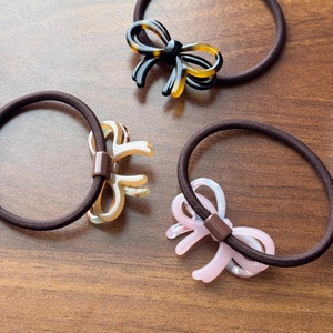Three-piece acetate bow hair ties in tortoiseshell and marble patterns on wooden surface