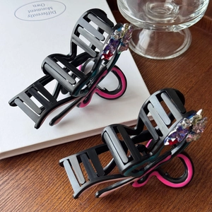 Elegant black and pink bow hair claw clips with colorful rhinestones on white book