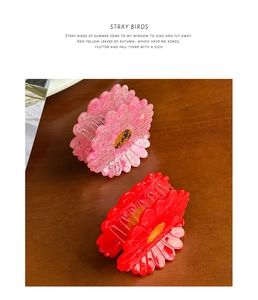 Detailed view of pink and red daisy-shaped acetate hair claws on a wooden background