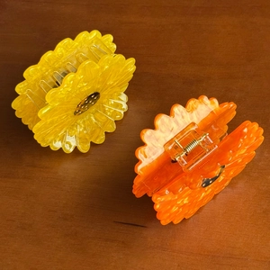 Cute acetate daisy flower hair claws in bright yellow and orange on wood surface