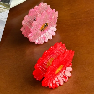 Daisy acetate flower hair claws in pink marble and red colors on a wooden background