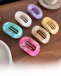 Flat oval hair claws with marble ink patterns displayed on dark wood surface