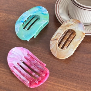 Trio set of marbled resin hair claw clips in blue, amber, and pink on wooden surface