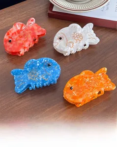 Detailed view of four colorful fish-shaped acetate hair claws on a dark wooden surface