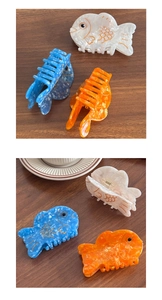 Detail of fish-shaped acetate hair claws in white blue and orange marble finish