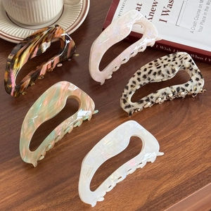 Five oversized acetic acid hair claws in marble and leopard patterns on a rustic desk