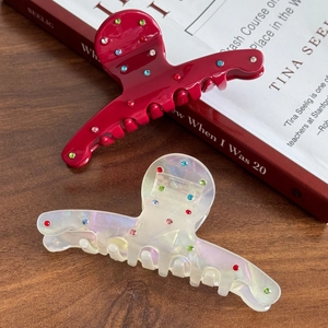 Elegant acetate hair claw clips with colorful rhinestones on a rustic wooden table