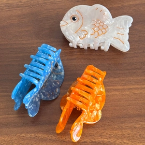 Fish-shaped acetate hair claws in white, blue, and orange on a wood background
