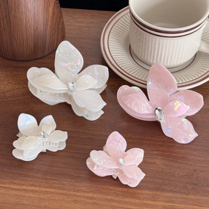 Iridescent flower hair claw clips with rhinestones in cream and pink on a wooden desk
