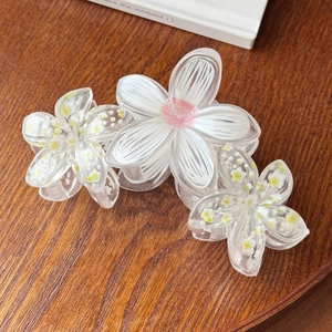 Close-up of floral hair claw clips with white and yellow patterns on a wooden surface
