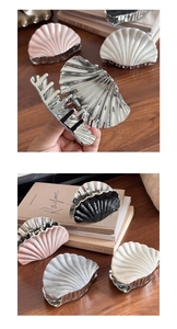 Detailed view of large shell-shaped hair claw clips in silver and pink on a desk
