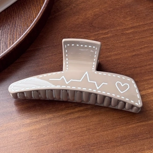 Detail view of khaki resin hair claw clip with white heart and pulse line patterns