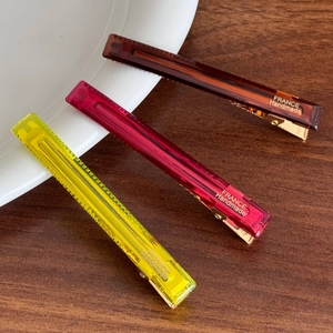 Drei durchscheinende bonbonfarbene Haarspangen auf Keramikteller mit goldenem Metallboden