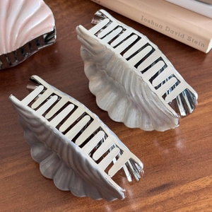 Elegant shell-shaped hair claws in silver metal with pearlescent finish on wooden desk