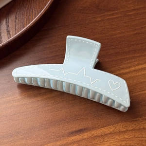 Detail of light blue hair claw clip with white stitching and heart pulse pattern