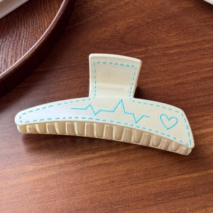 Detail of cream hair claw clip with blue heart and heartbeat line pattern on wood