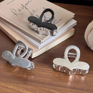 Elegant silver-plated heart claw clips in black, grey, and white on a wooden desk