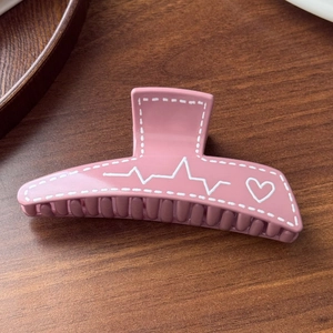 Detail of matte pink hair claw clip with white heart graffiti on a wooden surface