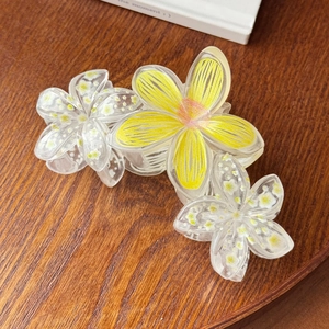 Detail of yellow flower hair claw clip with transparent petals on dark wooden background
