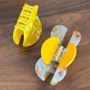 Elegant yellow marble and floral acetate hair claws on a dark wood background
