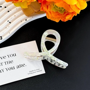 Close-up of a large white marble acetate hair claw clip on a ceramic tray with flowers