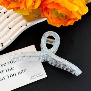 Detailed view of large translucent light blue claw clip with gold spring on black background