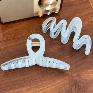 Translucent white marble hair claws with wave and cross designs on a wooden surface