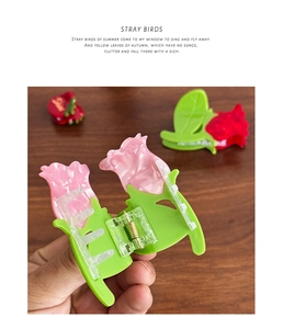 Détail d'une main tenant une pince à cheveux tulipe rose en acétate avec ressort doré