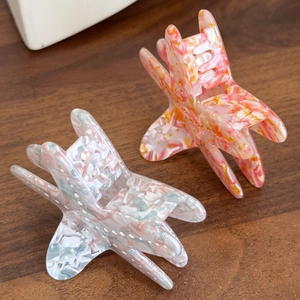 Star-shaped marble texture acetate hair claws with gold dot accents on wood surface