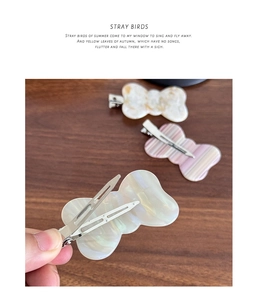 Detail of three acetate bow hair clips with pearlescent texture and metal duckbill clips