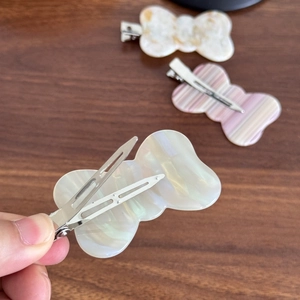 Three elegant bow-shaped acetate hair clips in marble and pearl patterns on wood background