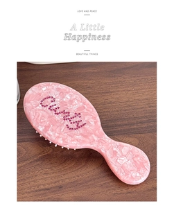 Detailed view of pink acetate hairbrush with rhinestone Care lettering on dark wood