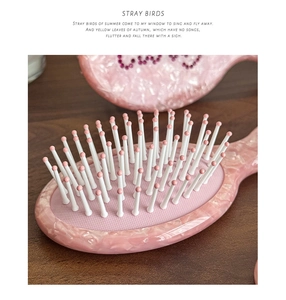 Close-up of pink marble pattern air cushion hairbrush with lucky rhinestone lettering
