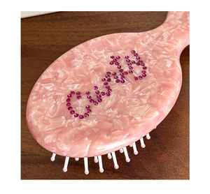 Detailed macro view of pink marble acetate hair brush with rhinestone logo embellishment