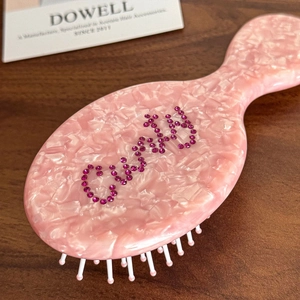 Pink marble acetate hairbrush with Curly rhinestone lettering on a wooden surface