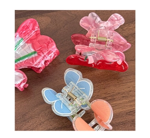 Three colorful butterfly hair claws in floral, pink, and blue acetate on a wood surface