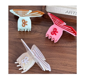 Close-up of three butterfly hair claws in mint, pink, and white on a wood surface