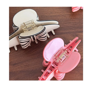 Detail view of bow hair clips in cream and pink stripes on a wooden surface