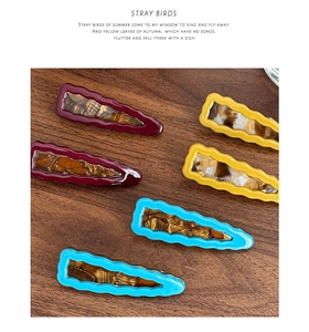 Detailed view of six resin hair clips in burgundy, yellow and blue on a wood background