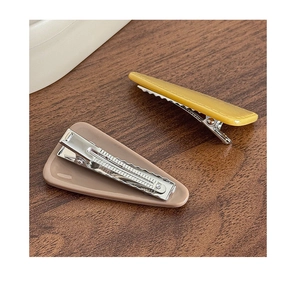 Close-up of minimalist ginger and beige hair clips on a textured wooden surface