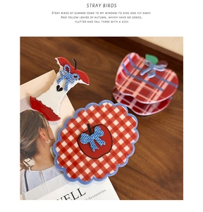 Detailed close-up of red and white plaid apple-shaped hair clips on a dark wood surface