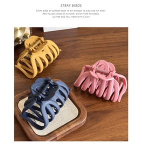 Three large matte hair claw clips in mustard, navy, and rose pink on a wooden desk